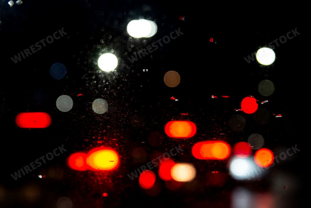 Colored lights blur through the car window, wet with raindrops. Heavy and slow traffic.