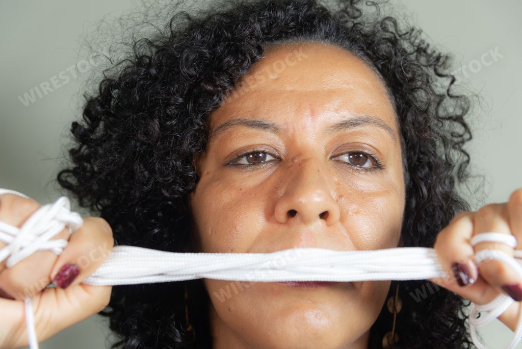 A closeup of the woman with black curly hair holding a bunch of white strings in front of her face.