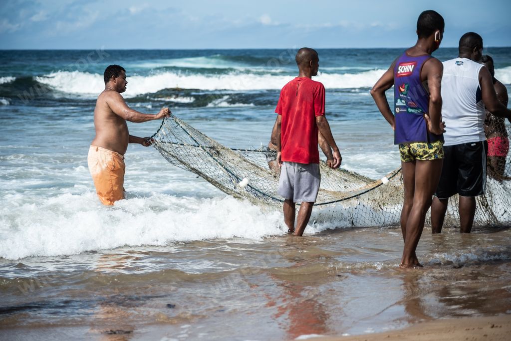 A group of Fishermen pulling the fishing net from the sea with fish inside. Boca do Rio beach