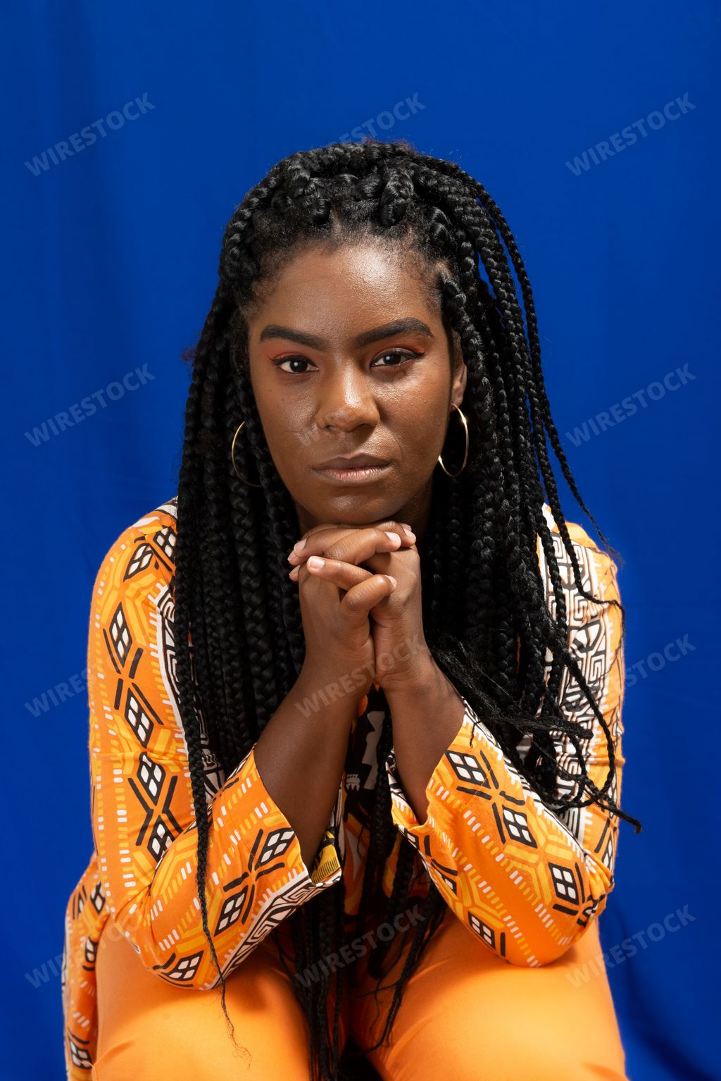 Close-up portrait of an Afro-Brazilian woman with hands on chin against blue background. She wears African-style clothes.
