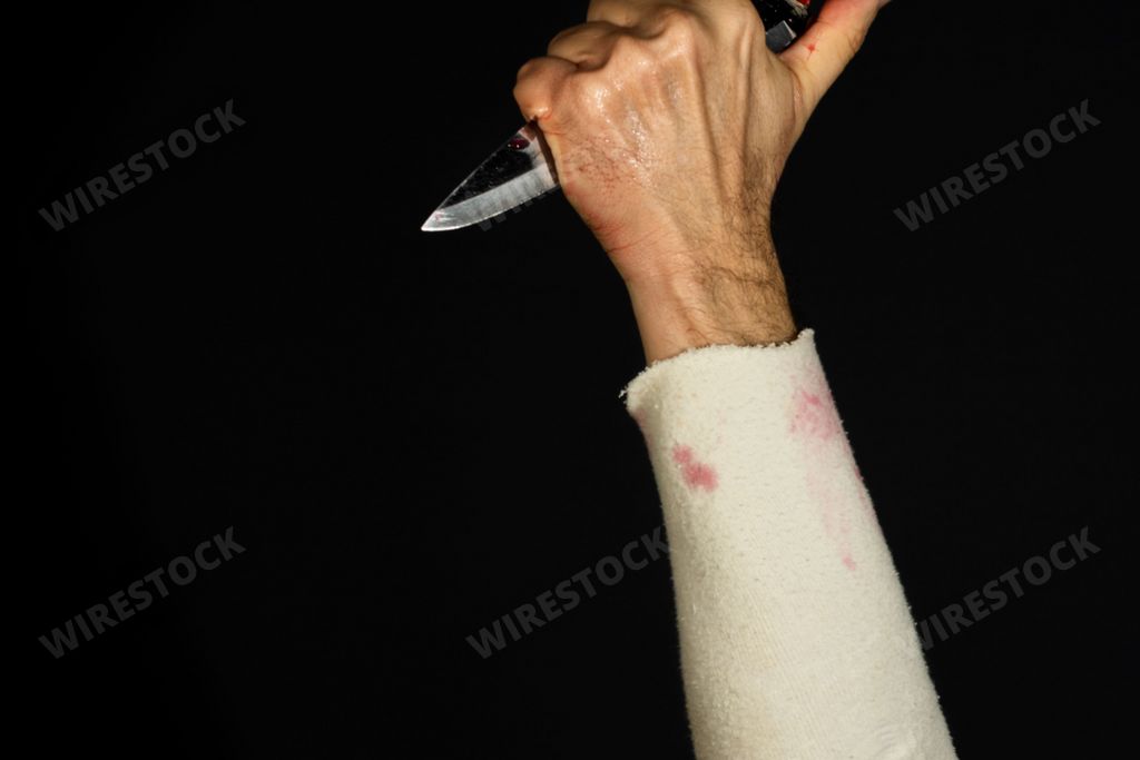 Hand holding knife stained with fake blood, against black background. Knife attack concept.
