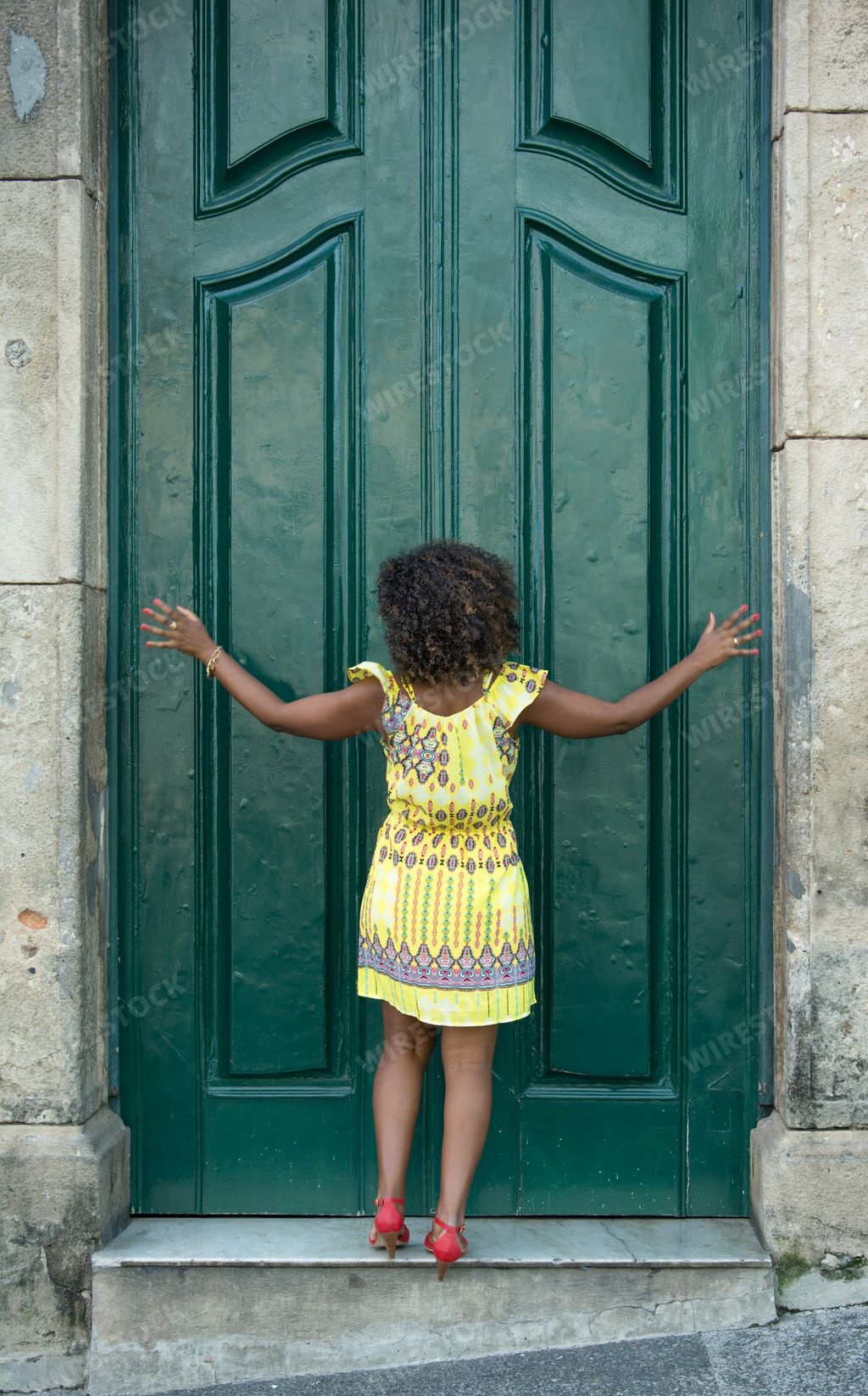 .A vertical shot of an African female model with curly hair dancing in front of a green door in Brazil