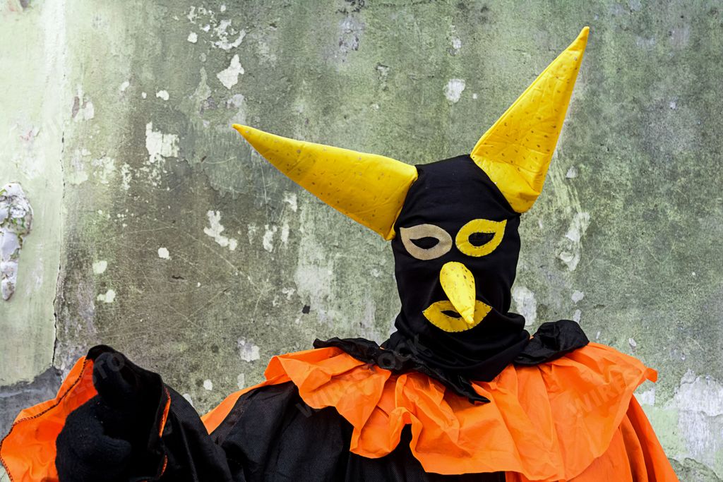 A jovial clown wearing a vibrant orange and black costume and a large, festive hat stands with arms outstretched in a welcoming gesture