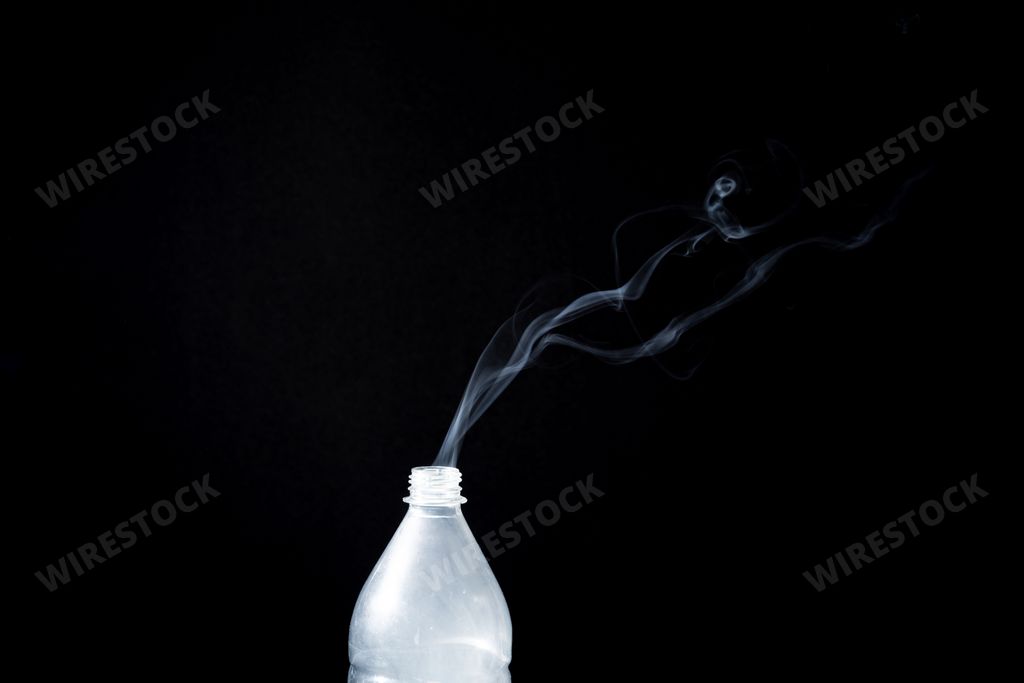 Smoke coming out of a plastic bottle against a black background with flare. Background for Halloween. Texture fog. Design element.