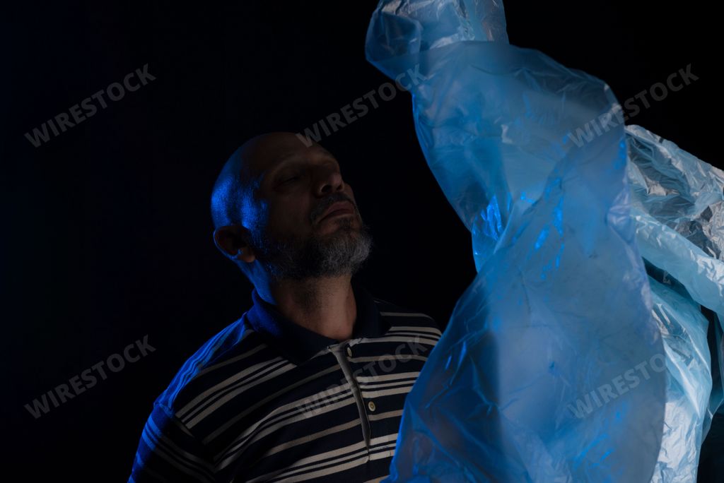 A sad bald mature man facing a transparent plastic bag flying over his head full of thoughts