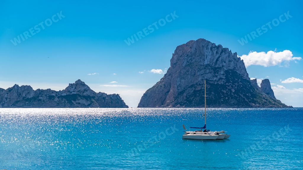 Ibiza, Cala dHort beach, beautiful sunny seascape with a sailboat and rocks in the sea
