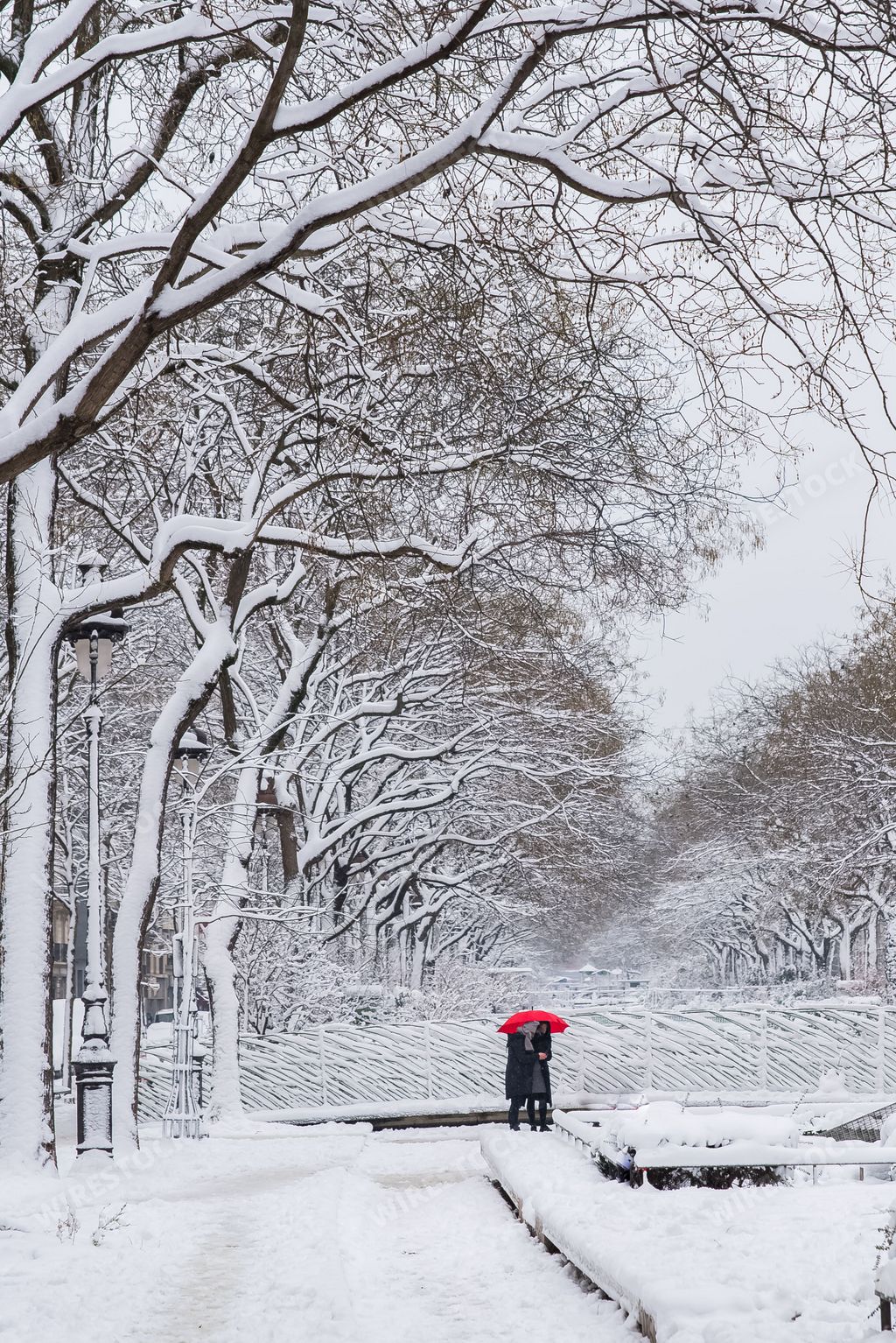Two people with red umbrella walking on white snow-covered  boulevard Richard-Lenoir in Paris