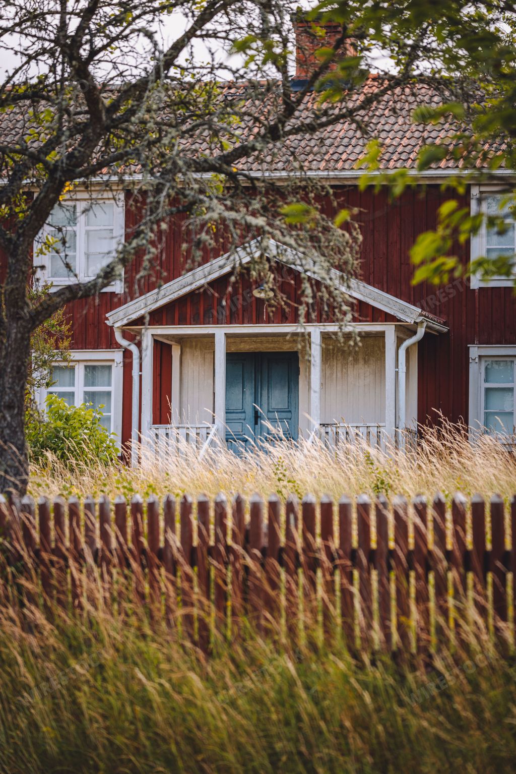 A vertical shot of an old red wooden house facade surrounded by trees and grass