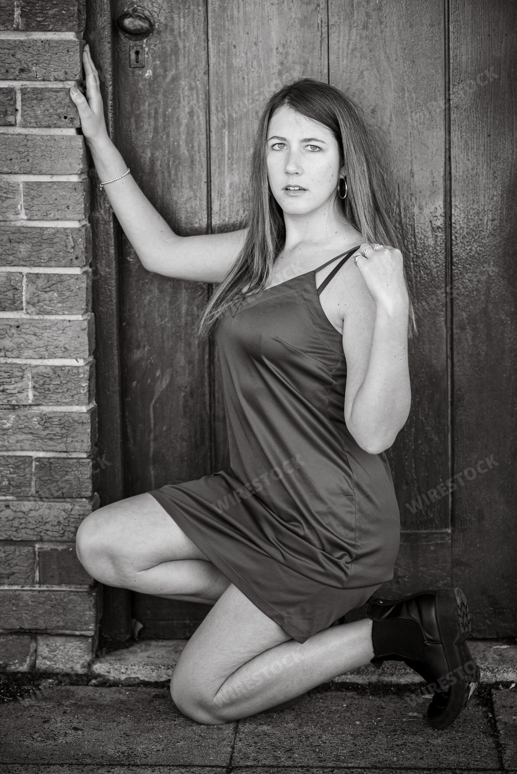 A brunette girl in a dress and boots kneeling in a doorway in grayscale