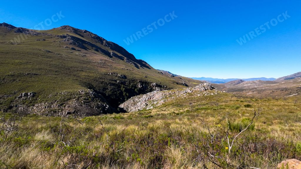 A scenic view of a grassy mountain landscape under a clear blue sky. South Africa