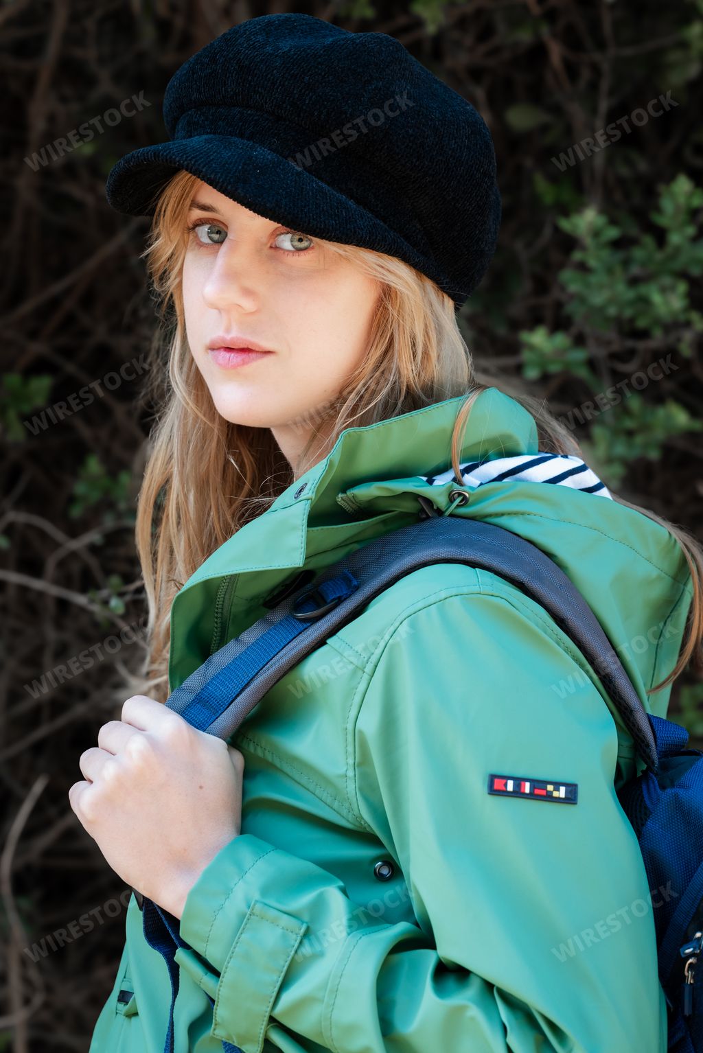 A blonde girl with a dark hat, warm jacket, and backpack looking at the camera