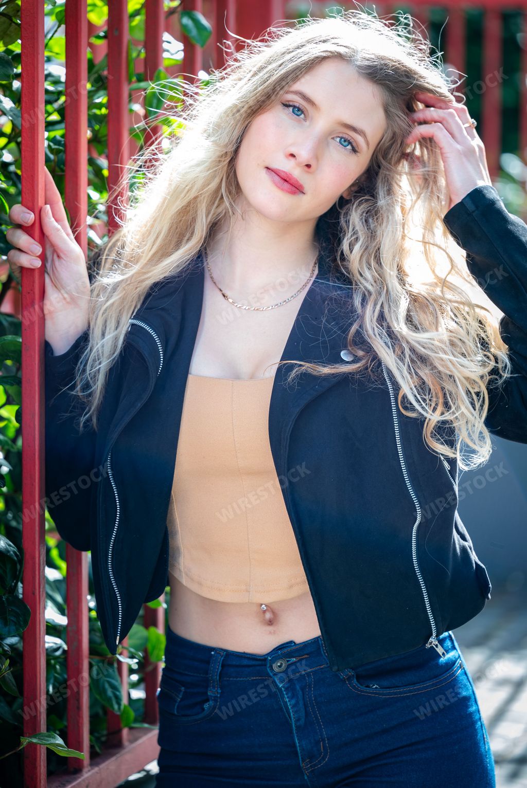 A closeup of a Blonde girl in a black jacket standing next to a red metal fence