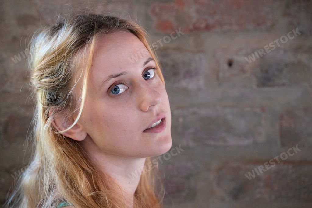 A closeup of a blonde girl against a brick wall