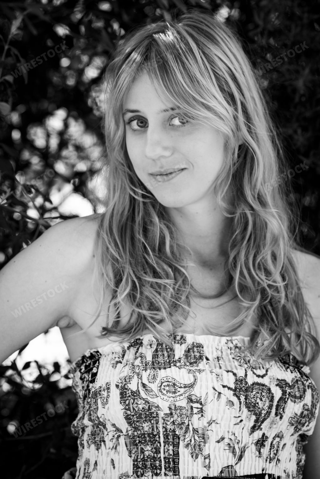 A Grayscale photo of a blonde girl leaning against a tree