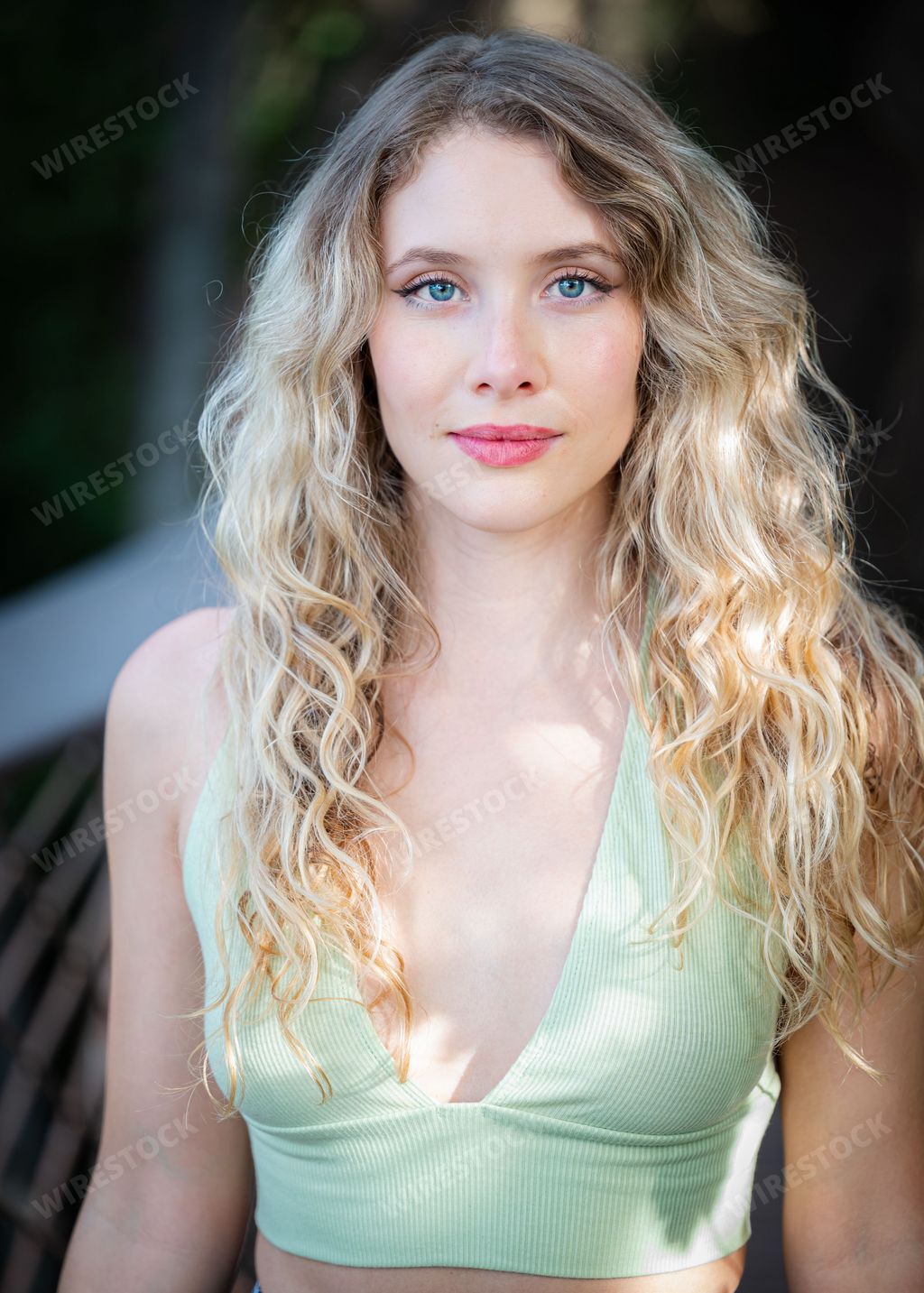 Happy young female with blonde hair and blue eyes wearing a green top, smiling and looking directly at the camera