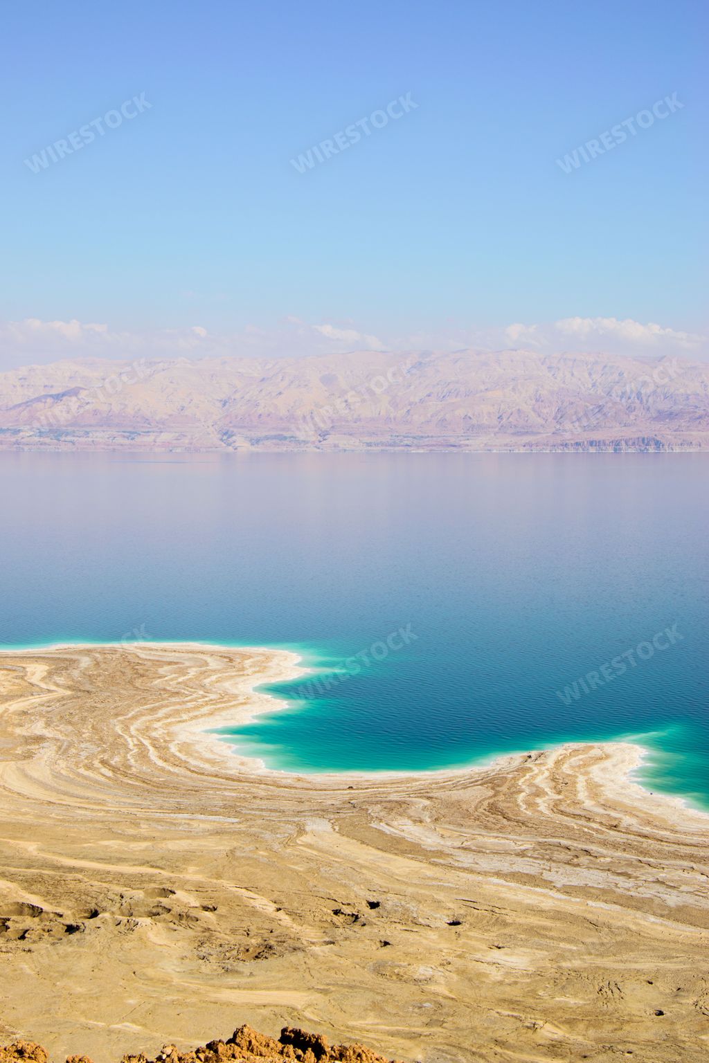 Aerial view of the Dead Sea from a rocky cliff, featuring the deep blue water and surrounding mountainside