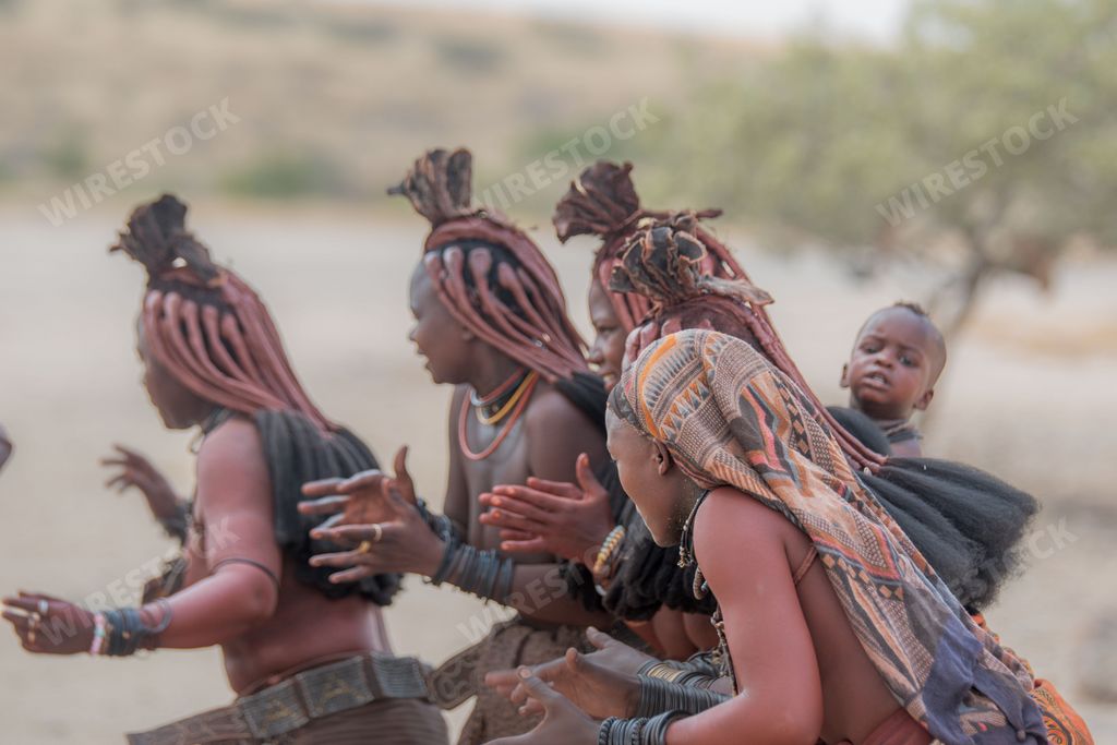 A group of Himba women in traditional attire running through a sandy landscape