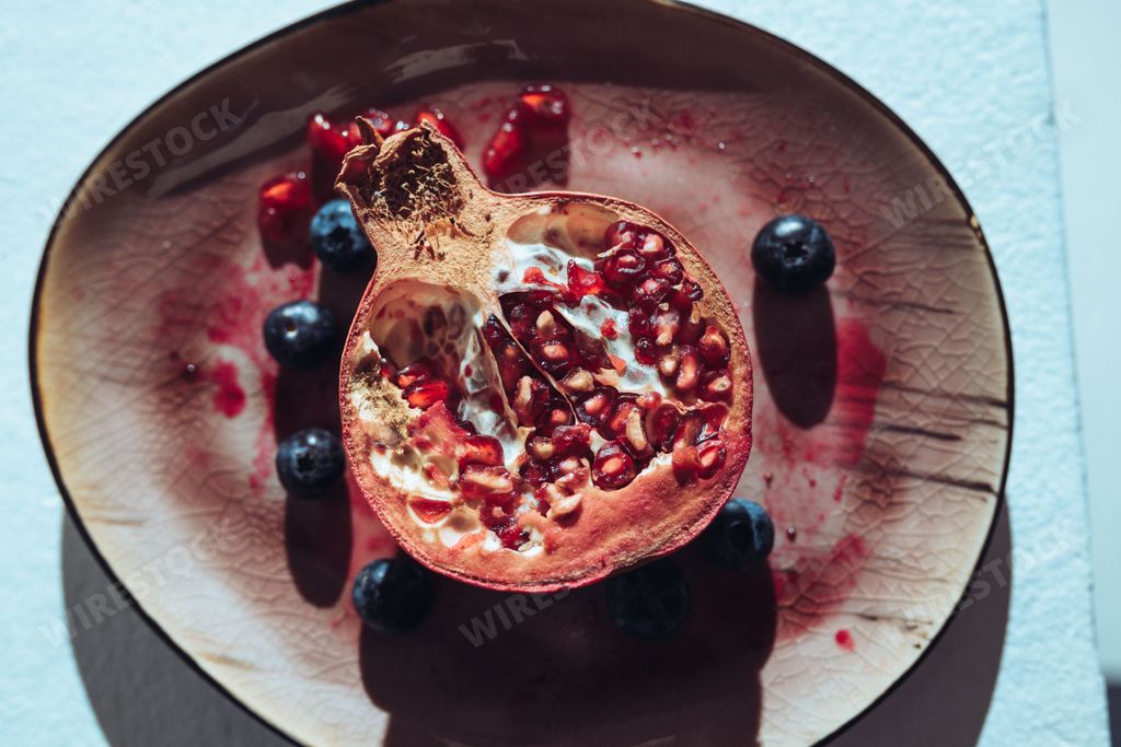A top view of a halved pomegranate with blueberries on a plate