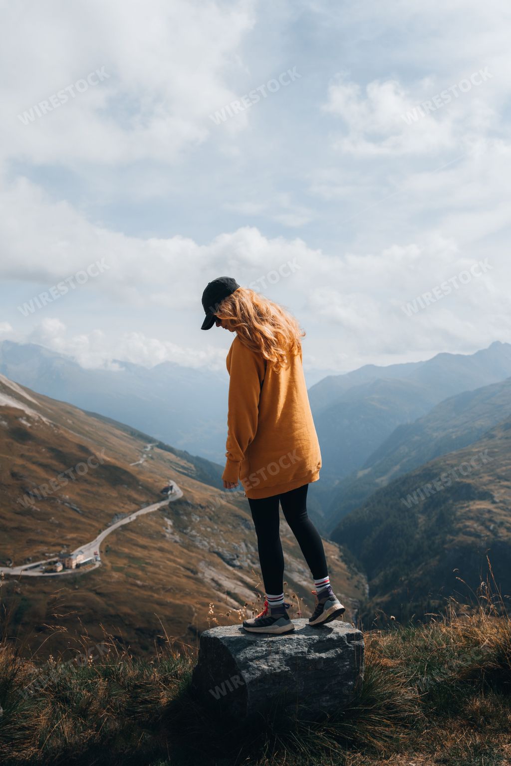A vertical shot of a blonde female hiker enjoying the view from a mountain near Grossglockner, Austria