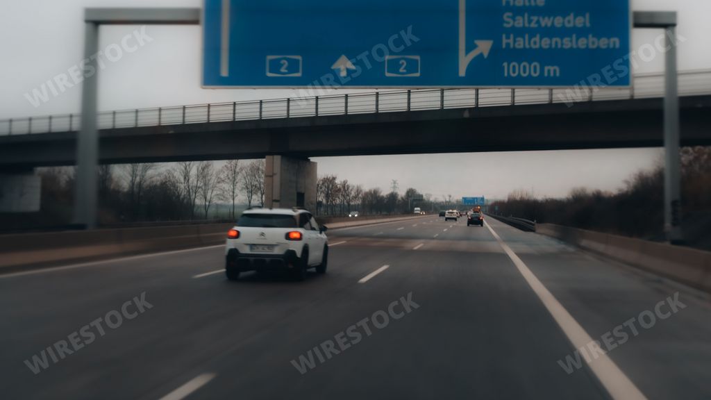 An overhead street sign positioned directly above a busy freeway, with two vehicles driving underneath