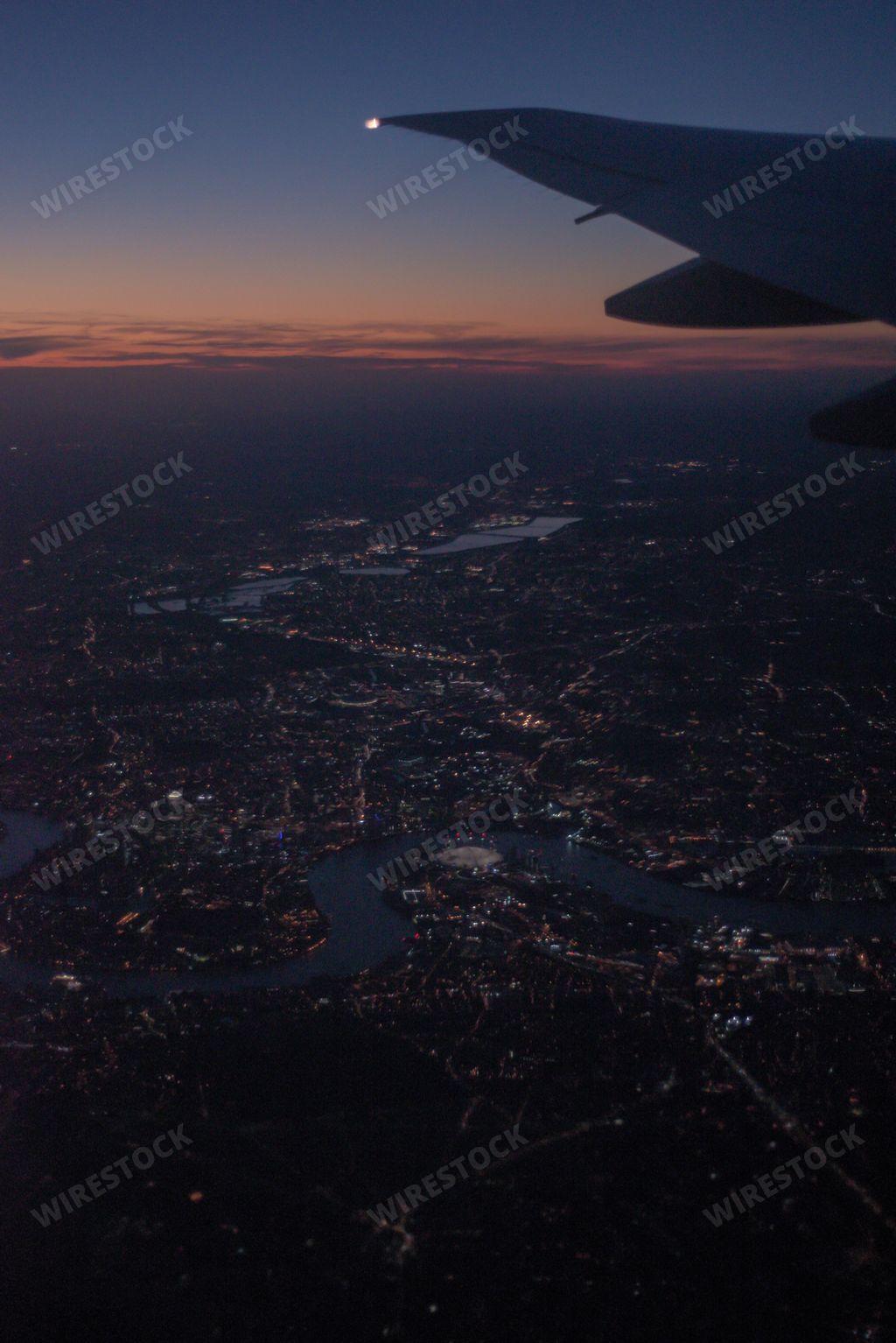 A vertical shot of an airplane flying over the city during sunset