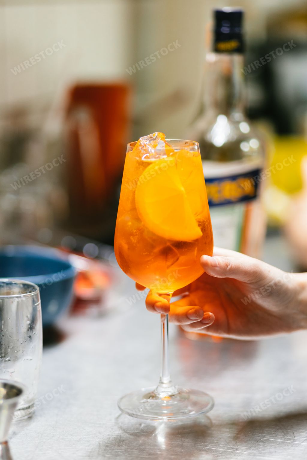 A vertical closeup of the hand preparing an Aperol Spritz drink.