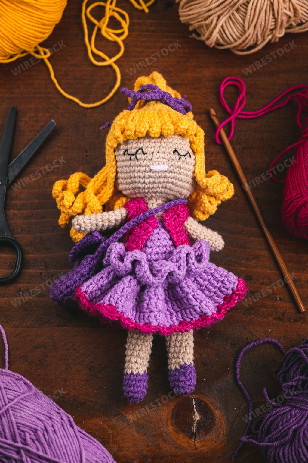 A vertical product photo of a handmade crochet toy doll for kids with its tools and materials
