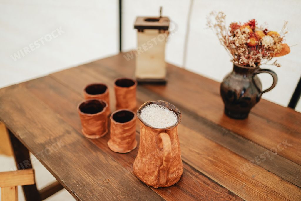 A closeup shot of handmade pottery cups with one full of mead beer on a wooden table
