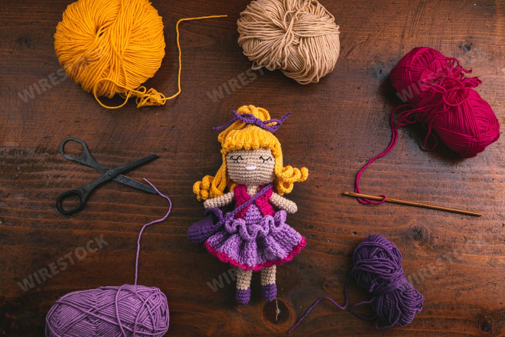 A product photo of a handmade crochet toy doll for kids with its tools and materials