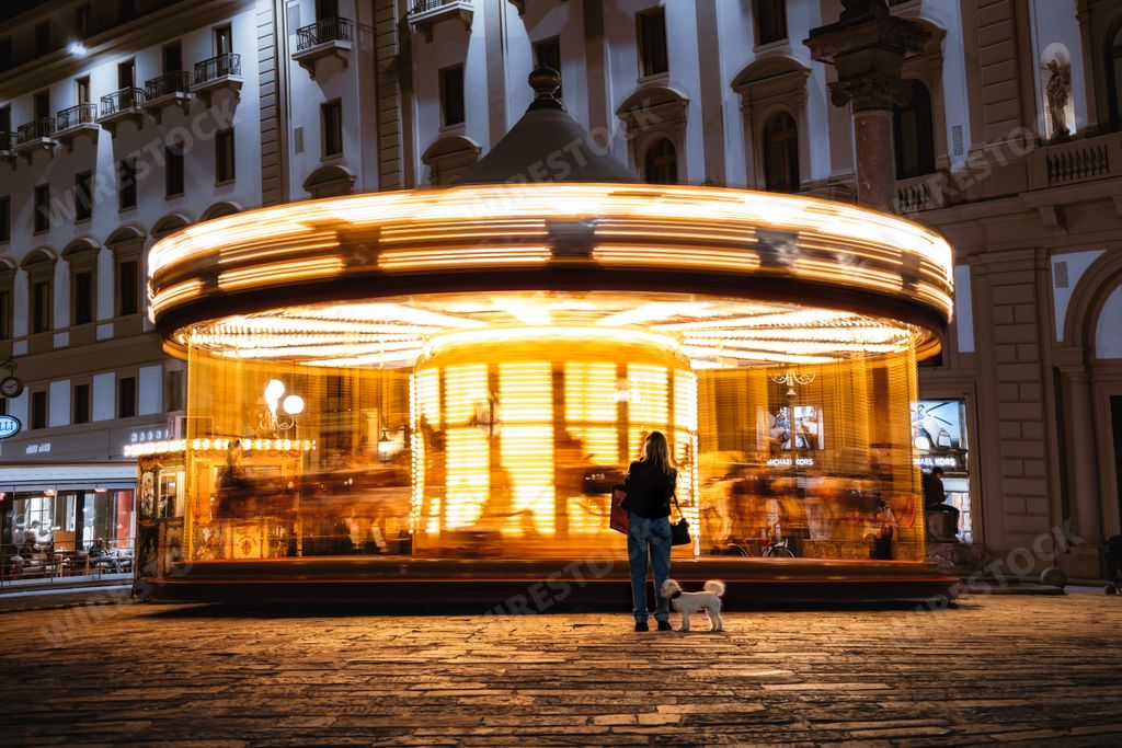 A woman with a poodle dog watching a carousel in Piazza Della Repubblica in Florence, Italy