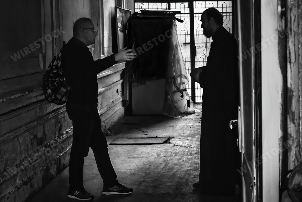 A grayscale shot of an angry man is angry at a priest in a dark alley.