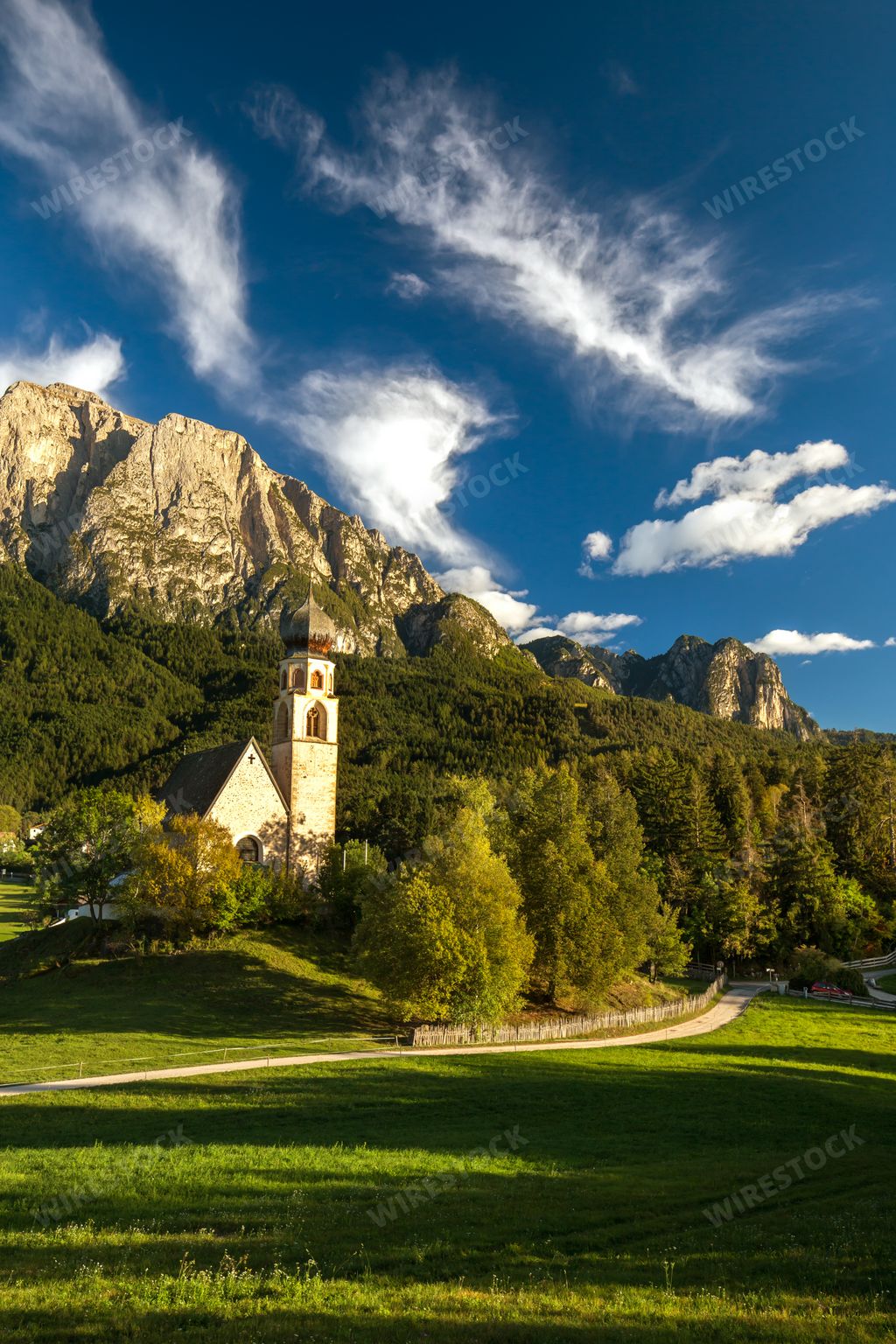 A vertical picture of a church surrounded by rocks covered in greenery under the sunlight in Italy