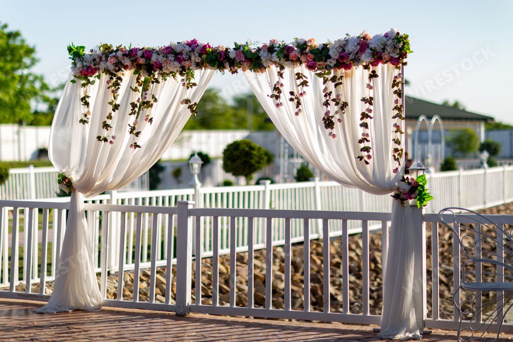 A beautiful wedding arch decorated with white cloth and colorful flowers on the wooden fence at the park