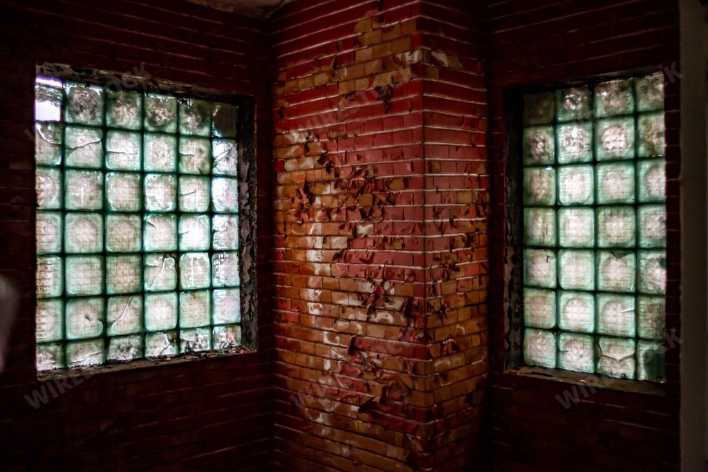 A red brick wall with glass windows in an abandoned building