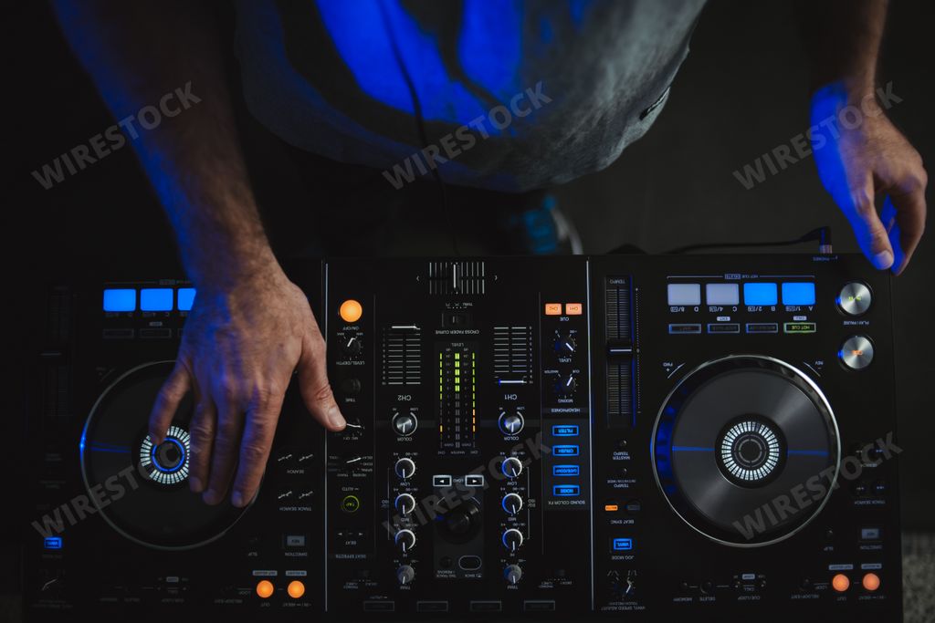 A closeup of a DJ working under the colourful lights in a studio