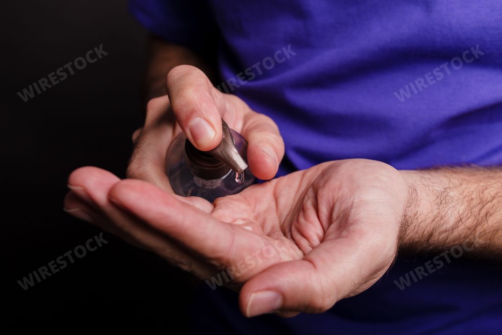 A closeup of a man using a hand sanitiser against a black background - COVID-19