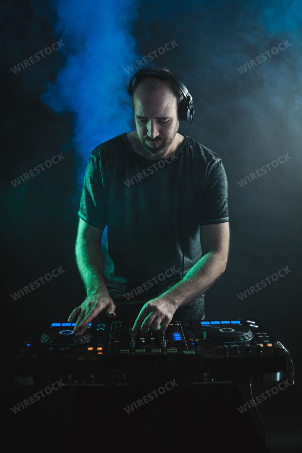 A vertical picture of a male DJ working under the lights against a dark background in a studio