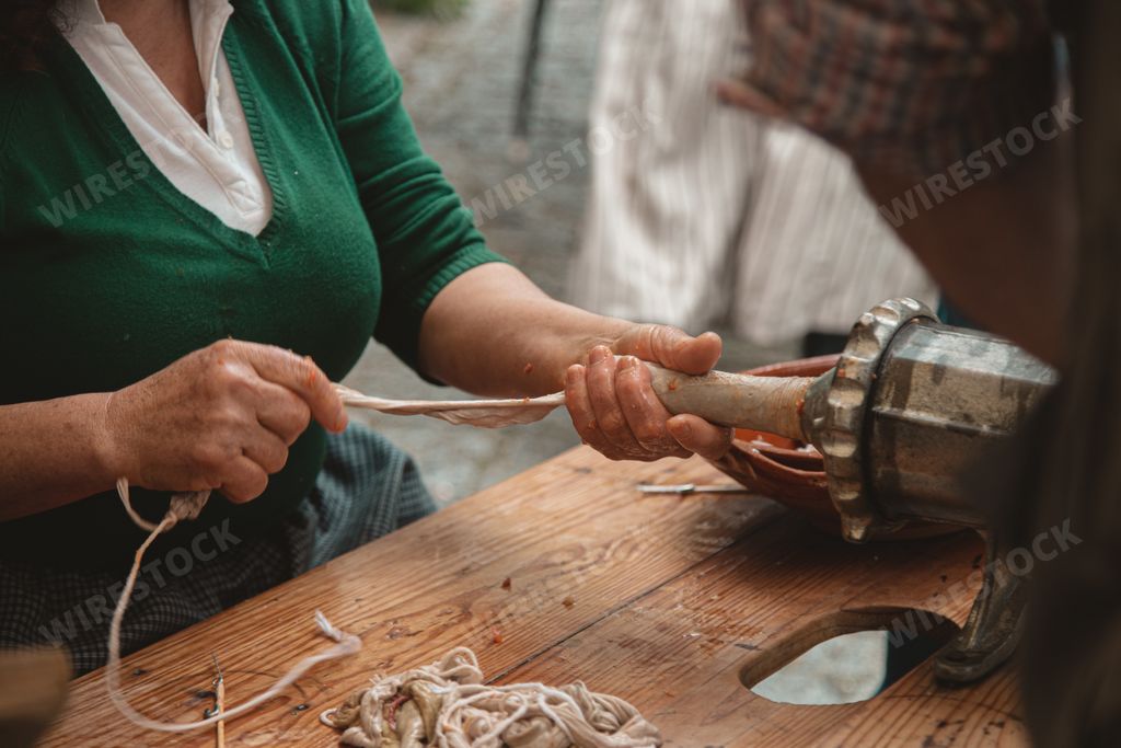 A picture of people preparing a kielbasa with an old-fashioned meat grinder on the wooden table