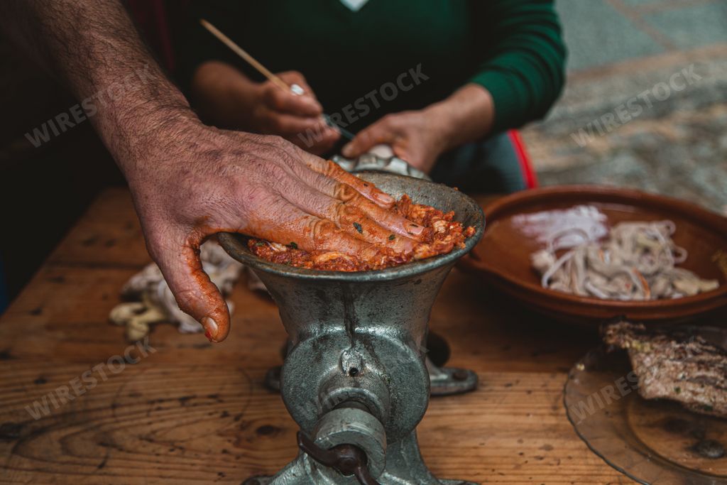 A closeup of a man grinding meat with an old-fashioned grinder on the wooden table