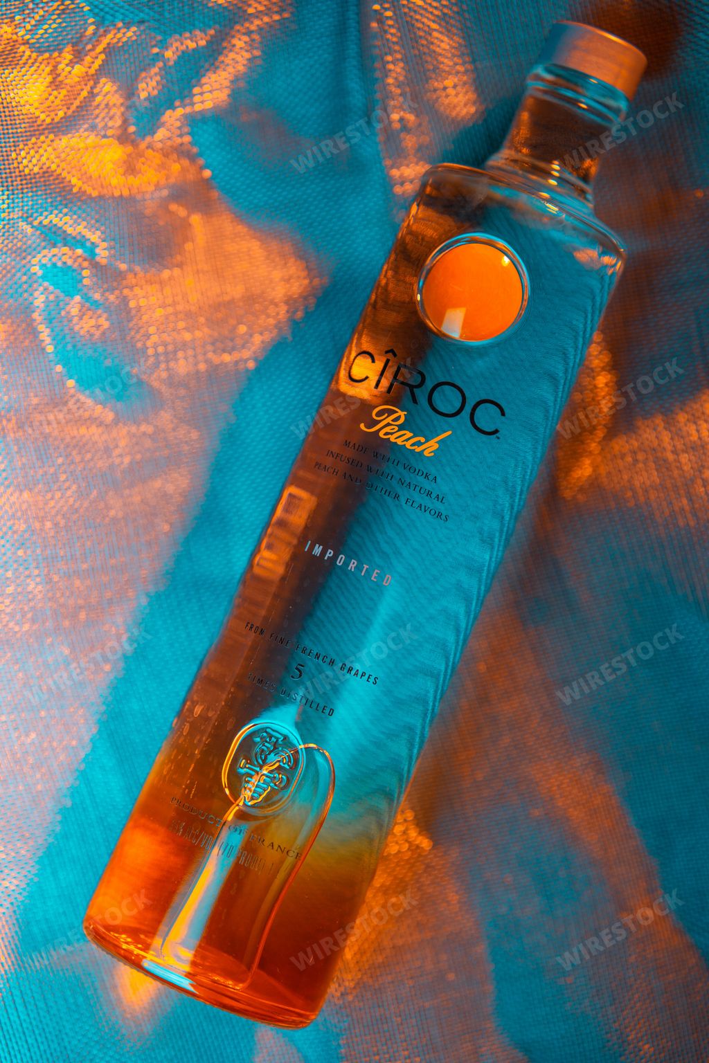 A vertical shot of a Ciroc Peach Vodka bottle under dim orange and blue lighting