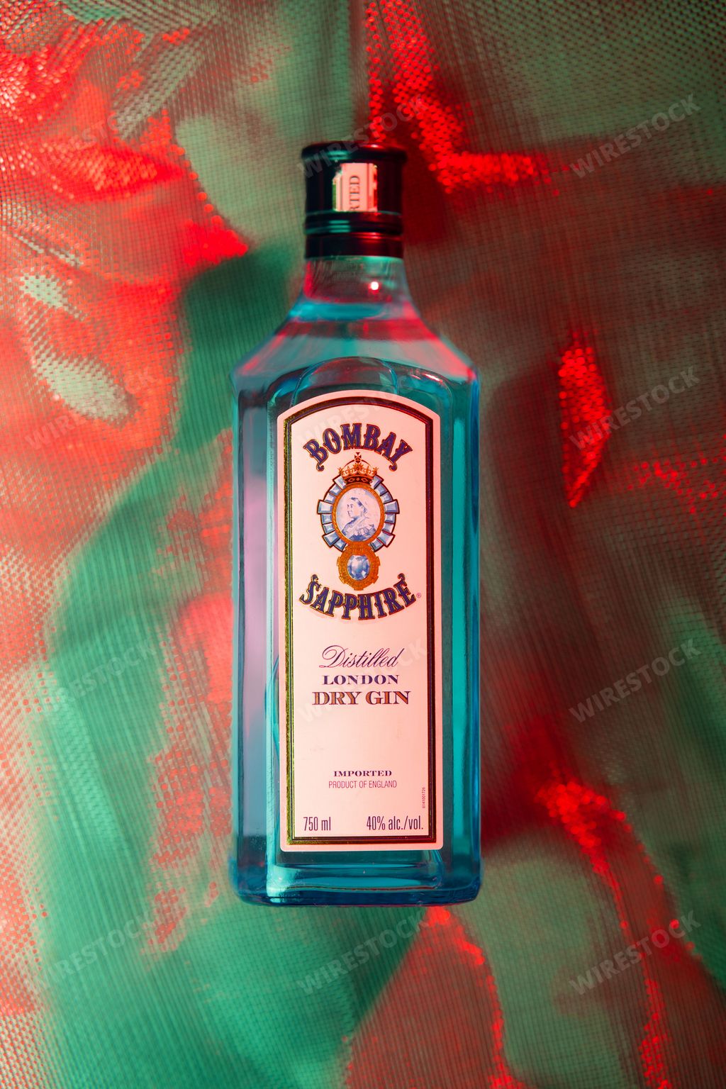 A vertical shot of a Bombay Sapphire Gin bottle under dim red and blue lighting
