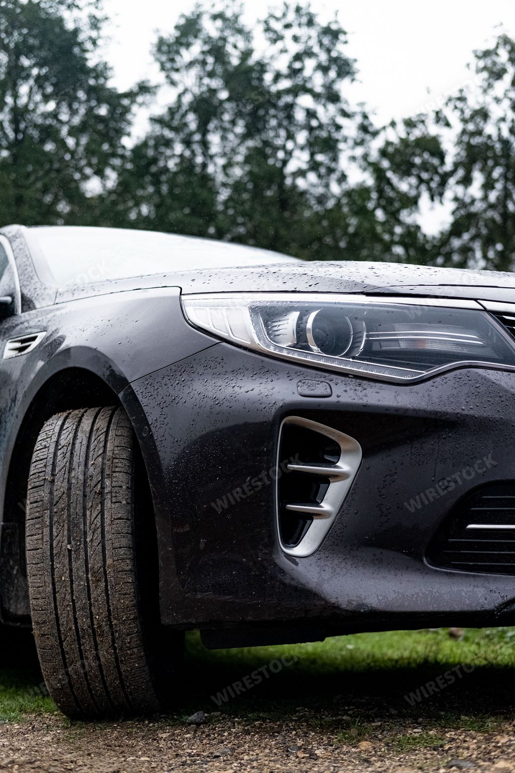 A vertical shot of a modern black car covered in rain