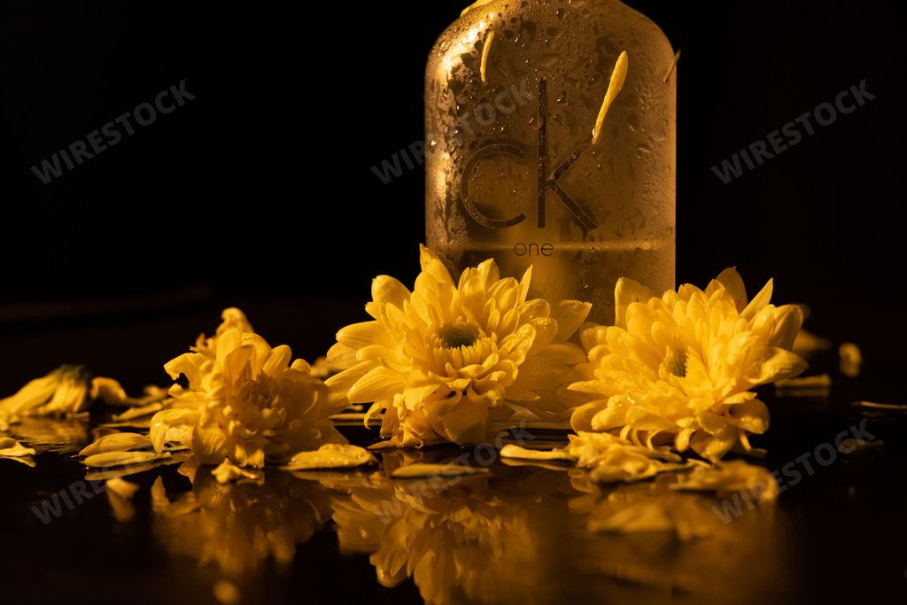 A bottle of the Calvin Klein Cologne For Men parfume with yellow flowers on a black background