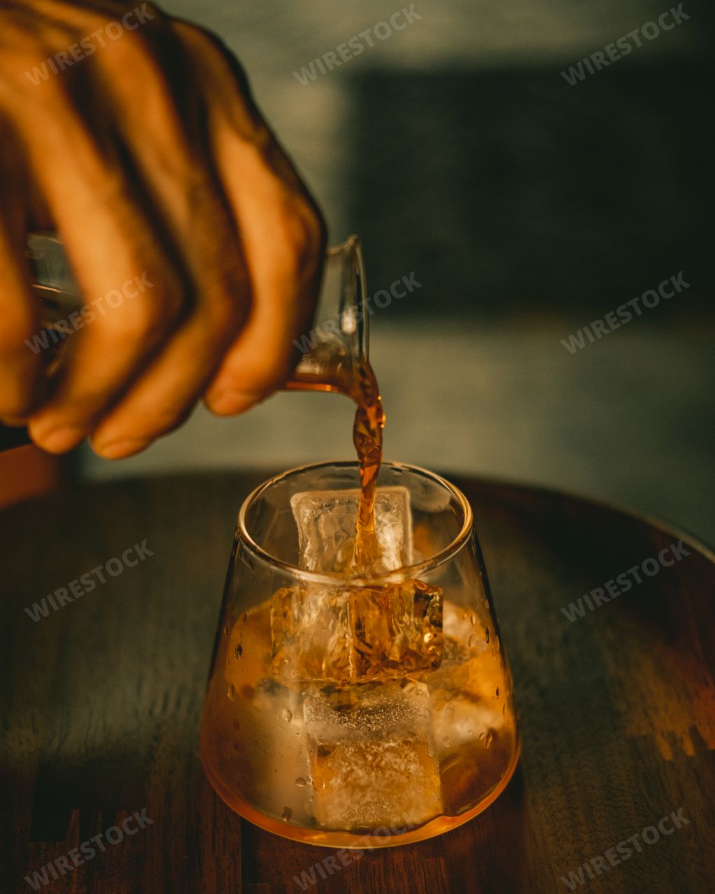 A vertical closeup shot of a hand pouring juice into a glass with ice cubes
