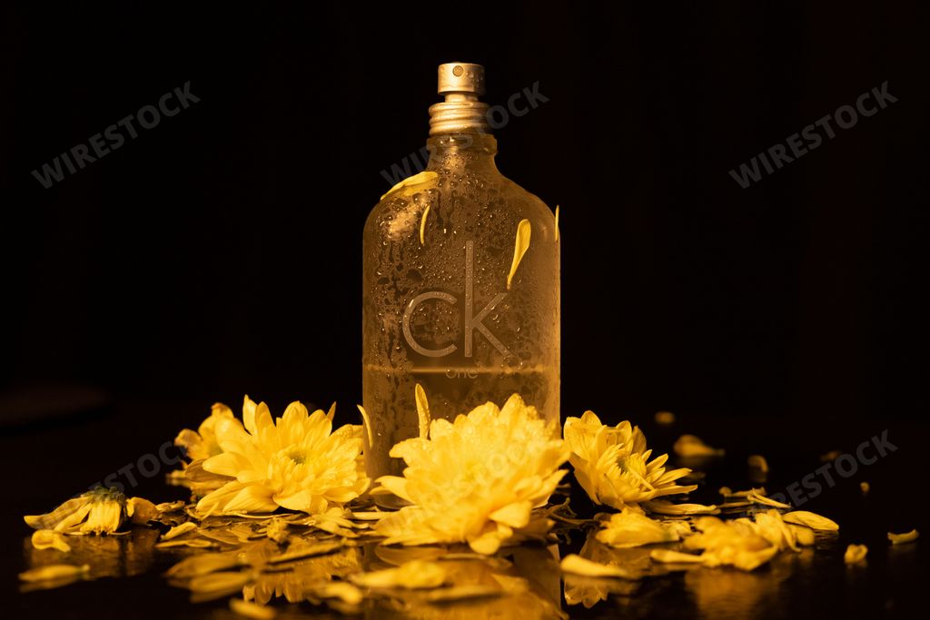 A closeup of Calvin Klein cologne with yellow flowers on a black background