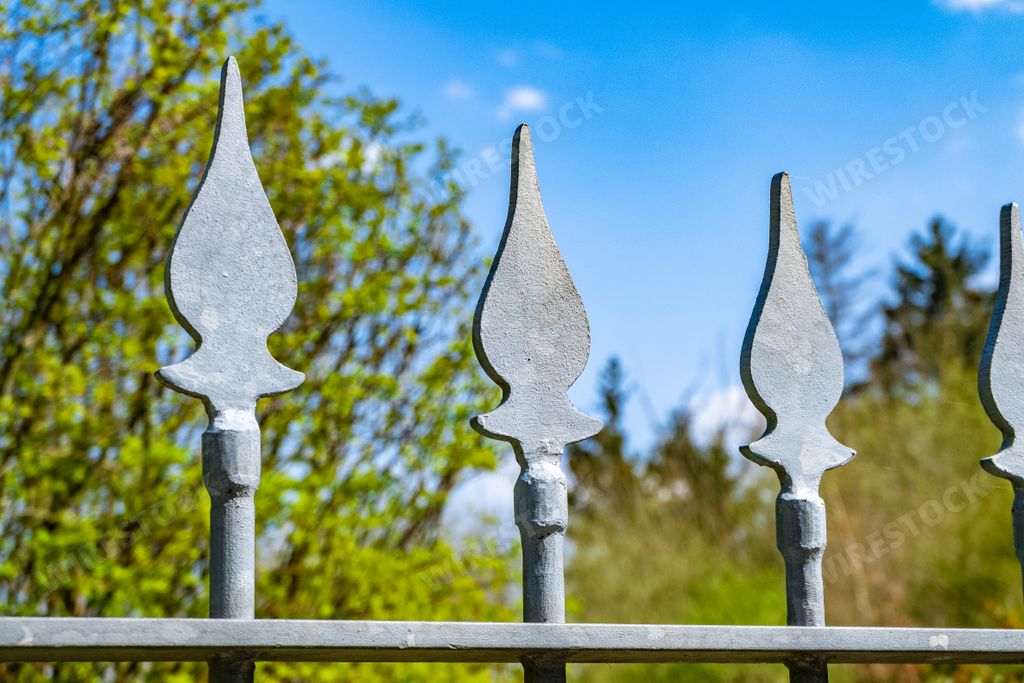 A closeup shot of the decorative fragments of an iron fence with blurry garden in the background
