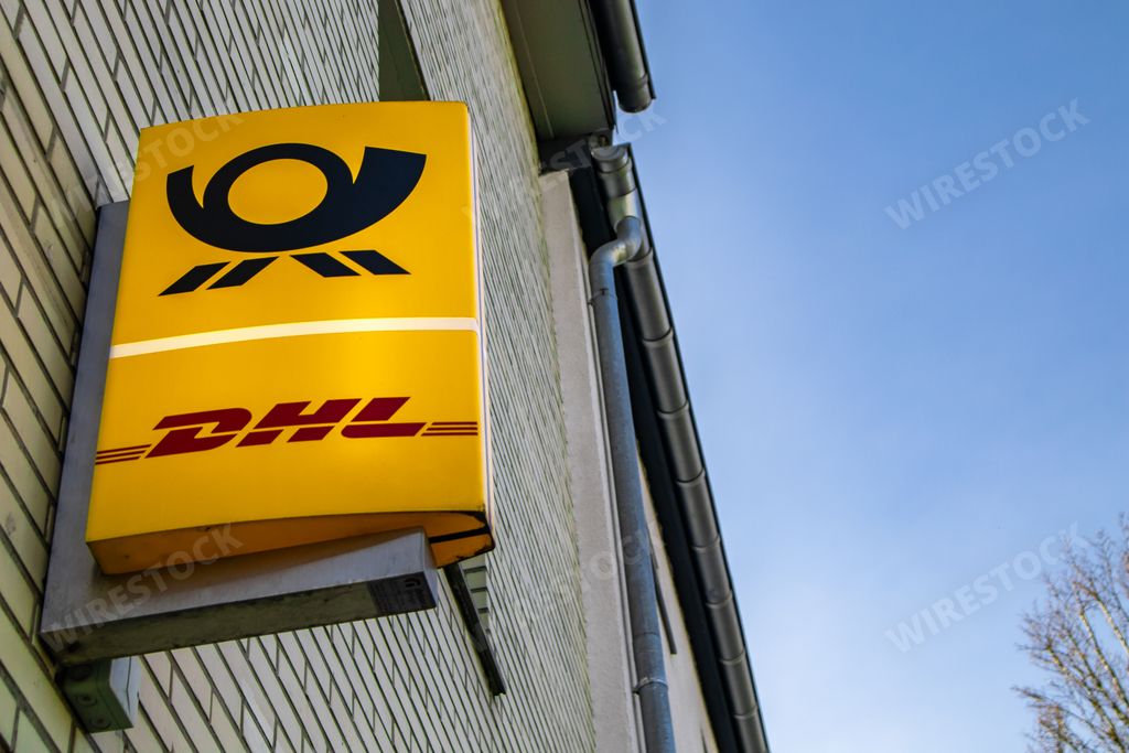 a bright luminous sign of dhl post service attached on a wall near the sidewalk