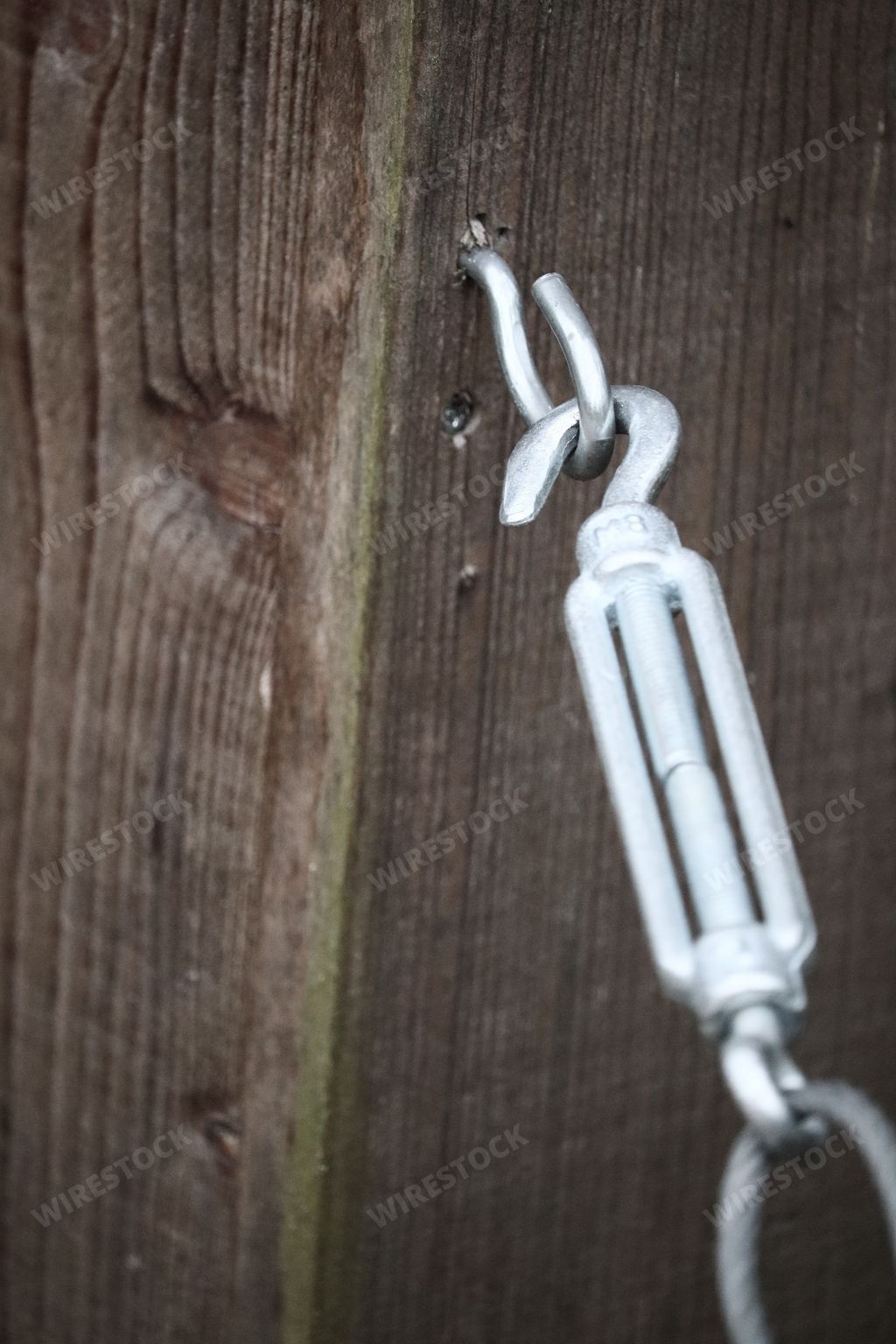 a metal hook fixated with a cable eyelet on a brown wooden fence