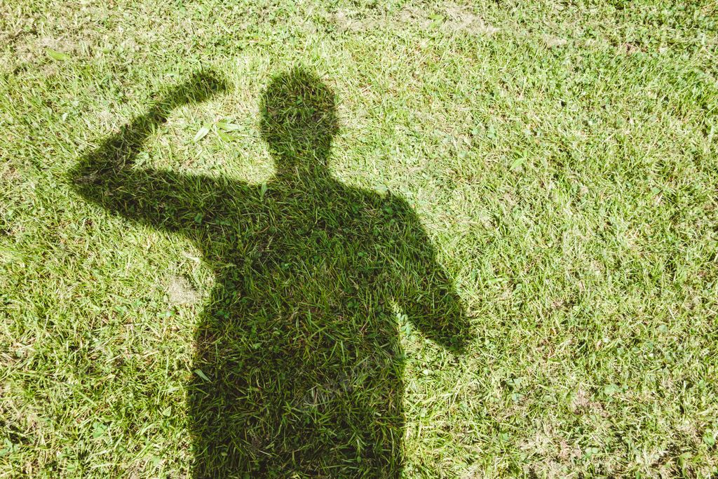 A high angle shot of the shadow of a person stretched on a grass-covered field