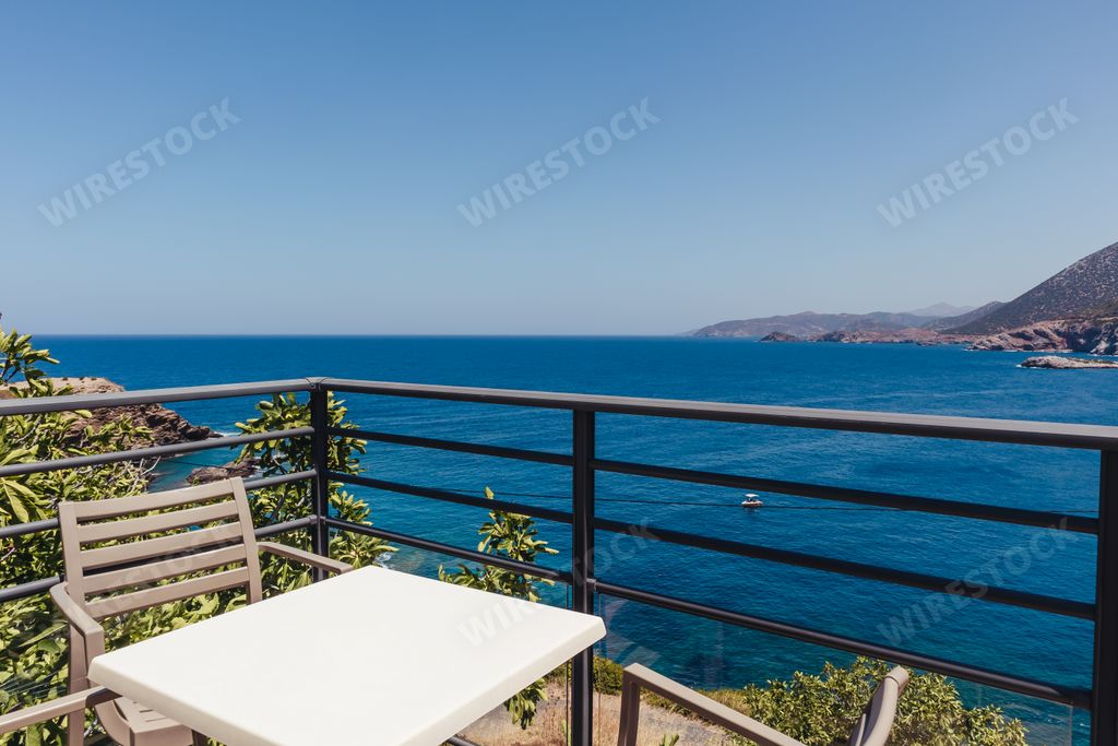Empty plastic chairs and tables at an outdoor cafe on a balcony with a view of the sea